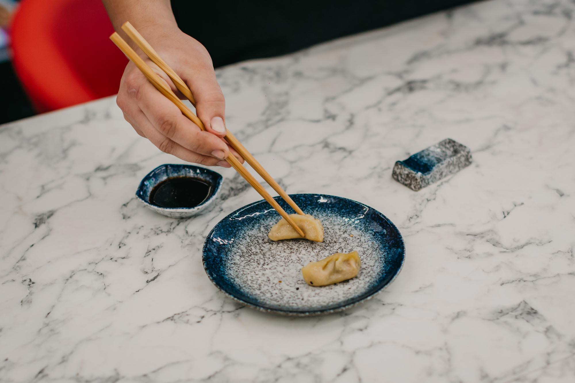 Close up of a person taking a cooked dumpling from a plate with chopsticks